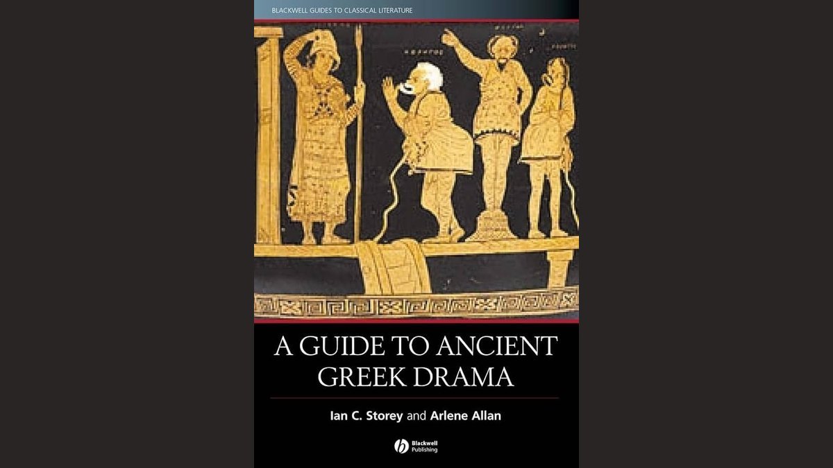An open classical drama book resting on a wooden desk near a theatrical mask.