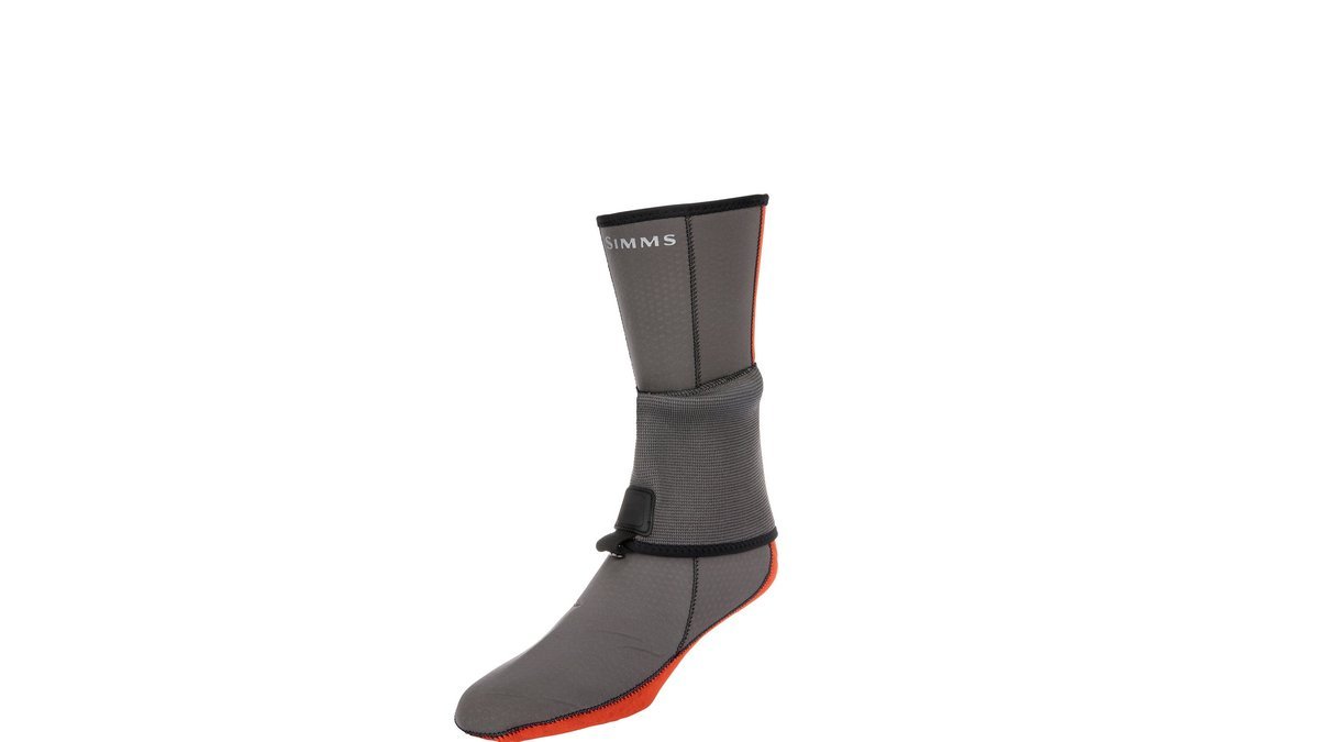 Rugged neoprene socks for fly fishing resting on a mossy river bank.