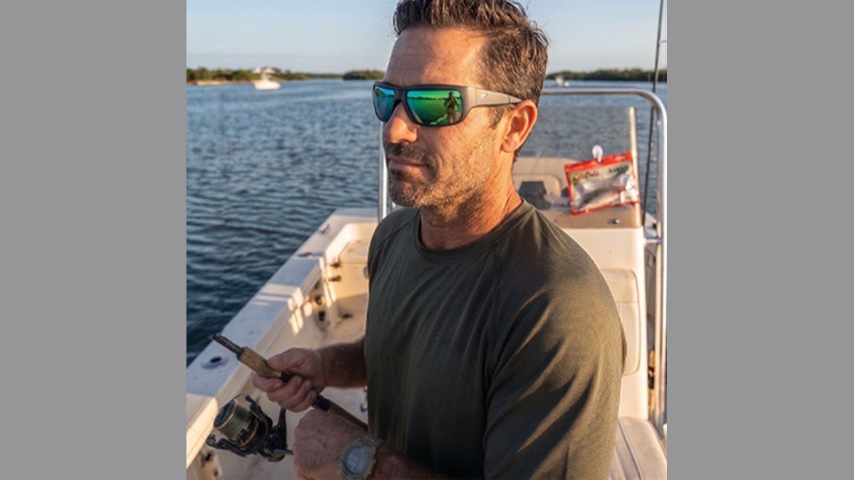 A pair of polarized sunglasses resting on a wooden boat deck overlooking a lake.