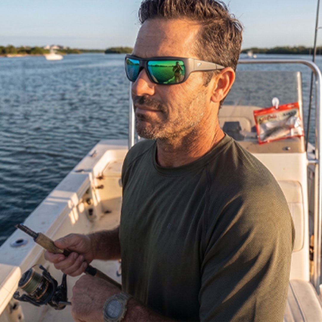 A pair of polarized sunglasses resting on a wooden boat deck overlooking a lake.
