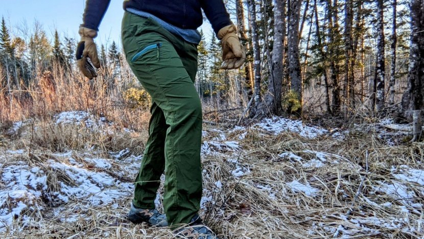 A tall woman wearing comfortable hiking pants stands on a scenic mountain ridge.