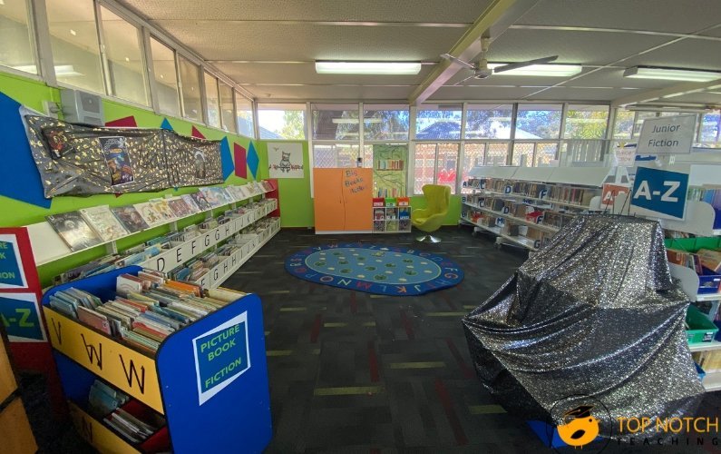 A stack of educational books rests on a table in a modern library.