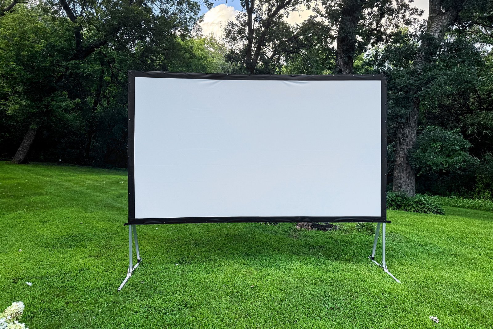 A portable outdoor projector screen stands in a backyard ready for an evening movie.