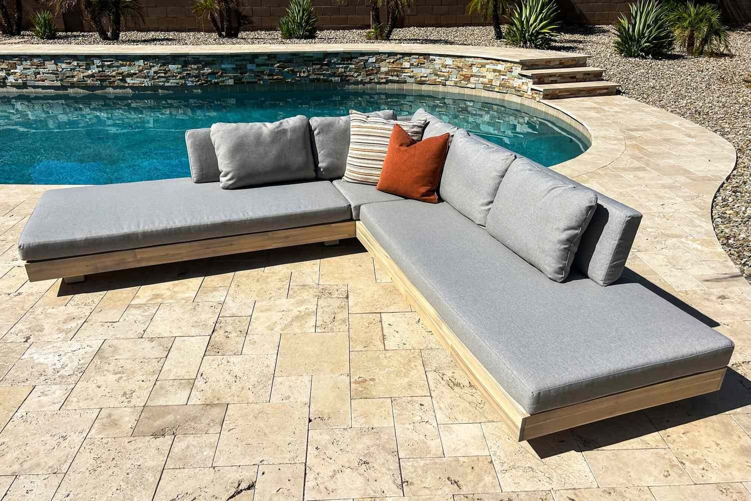 A modern outdoor sectional sofa sits on a stone patio in a backyard.
