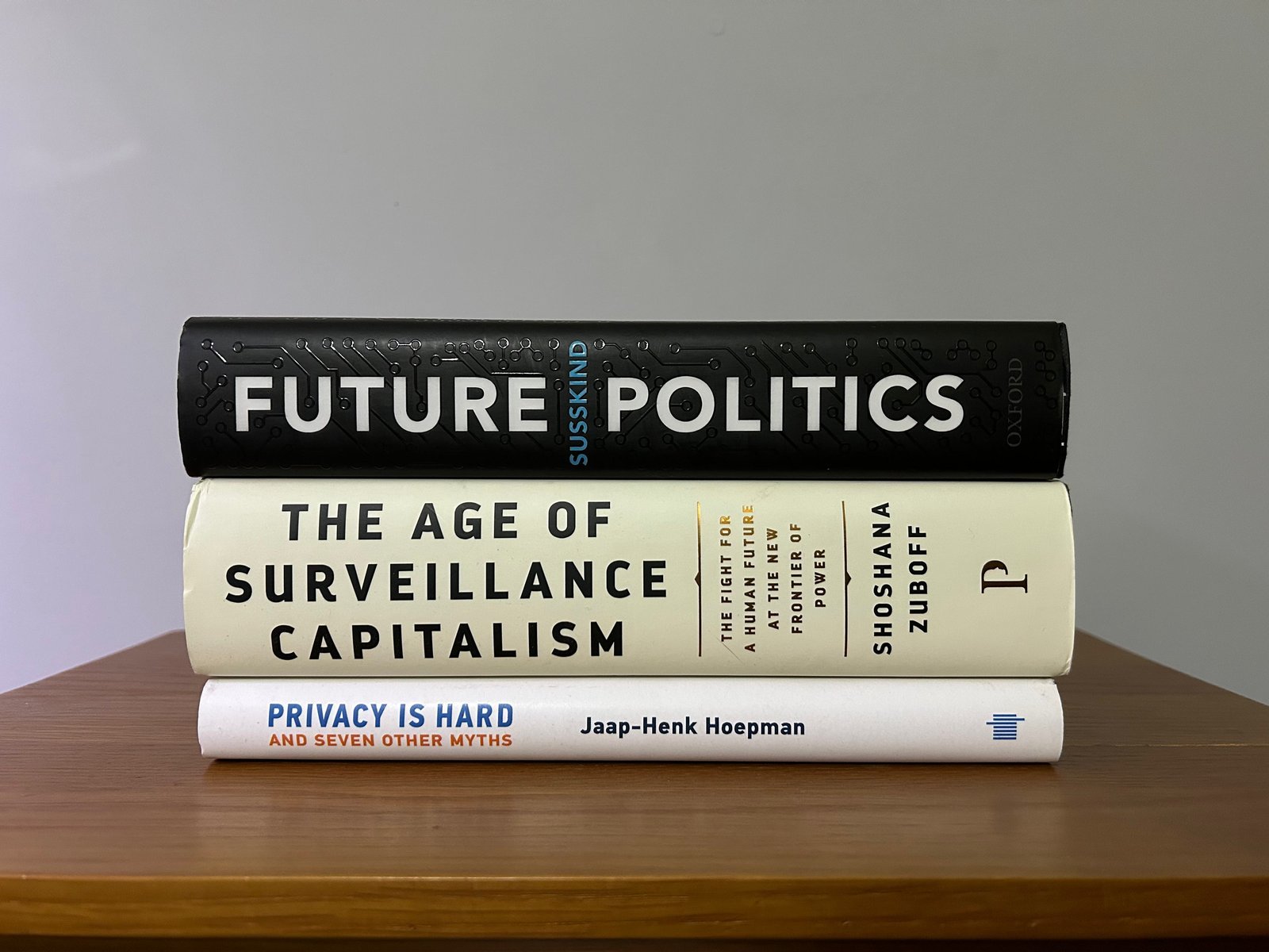 A stack of insightful books on privacy surveillance rests on a wooden table.