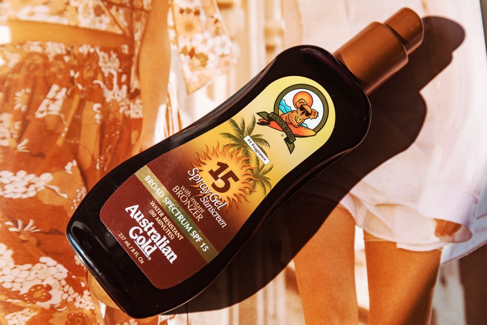 A bottle of premium suntan lotion sits on a wooden deck by a pool.