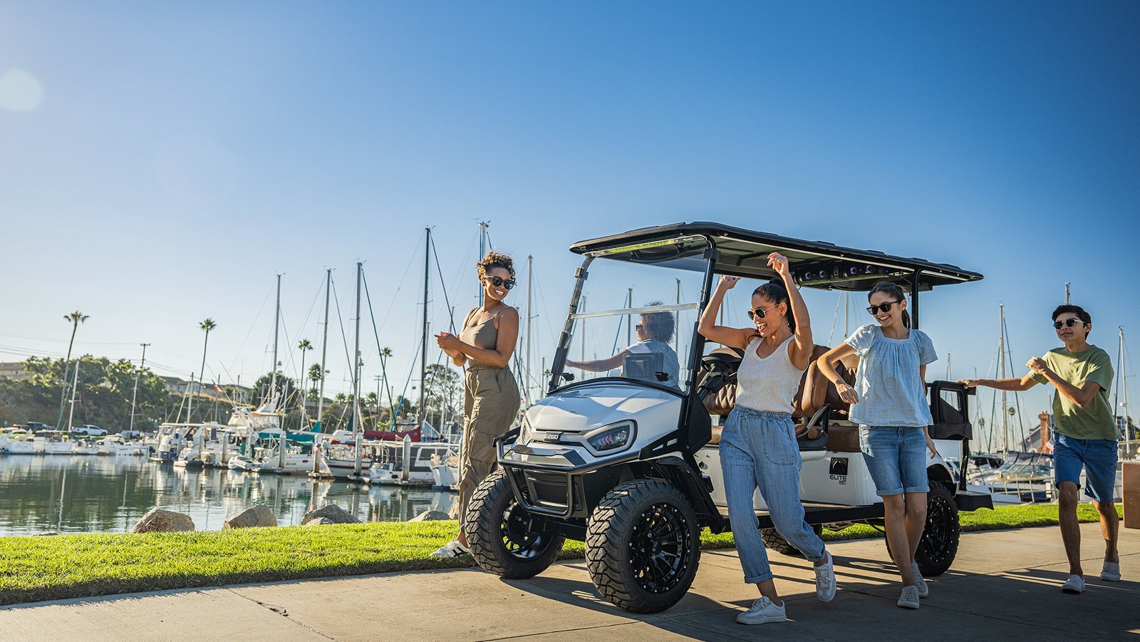 A clean E-Z-GO golf cart parked on a paved driveway near a course.