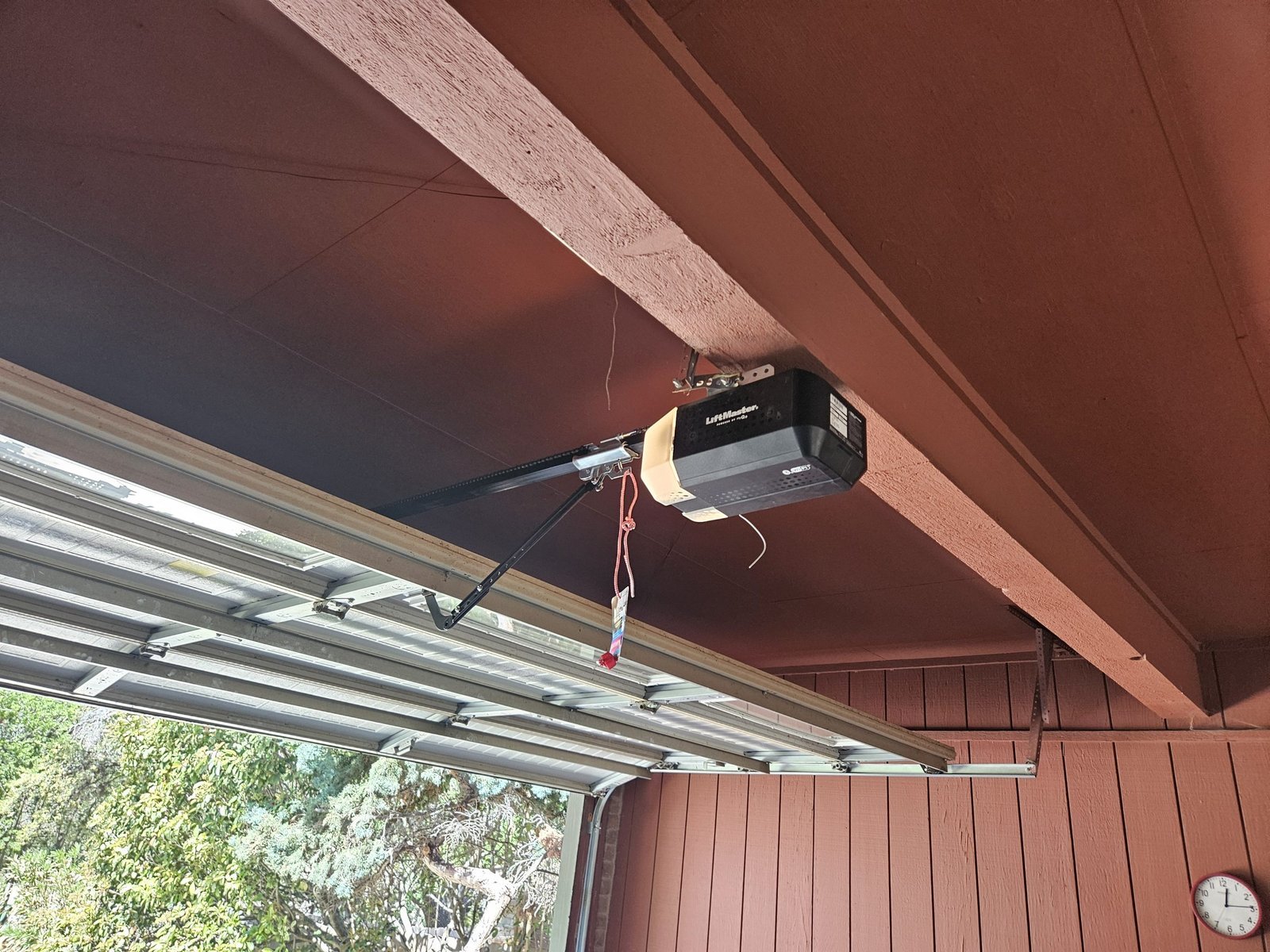 A hand pulling the red emergency release cord on a garage door opener.