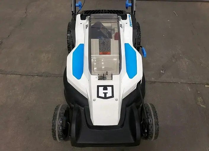 Hands pressing the thermal reset button on an electric lawn mower handle.