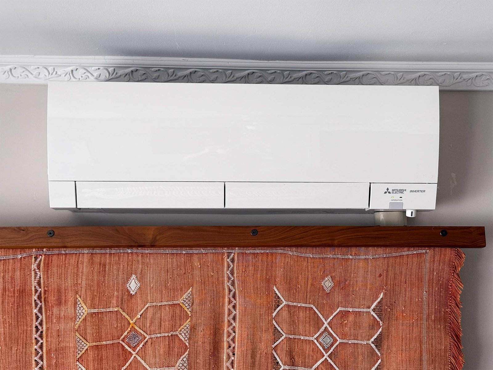 A wall-mounted mini split unit with airflow restricted by a nearby sheer curtain.