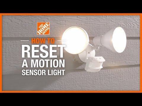 A dirty motion detector light sensor obstructed by debris on a white exterior wall.