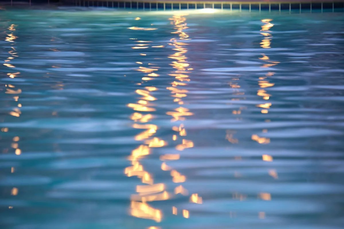 A technician carefully repairs an underwater pool light fixture on a pool deck.